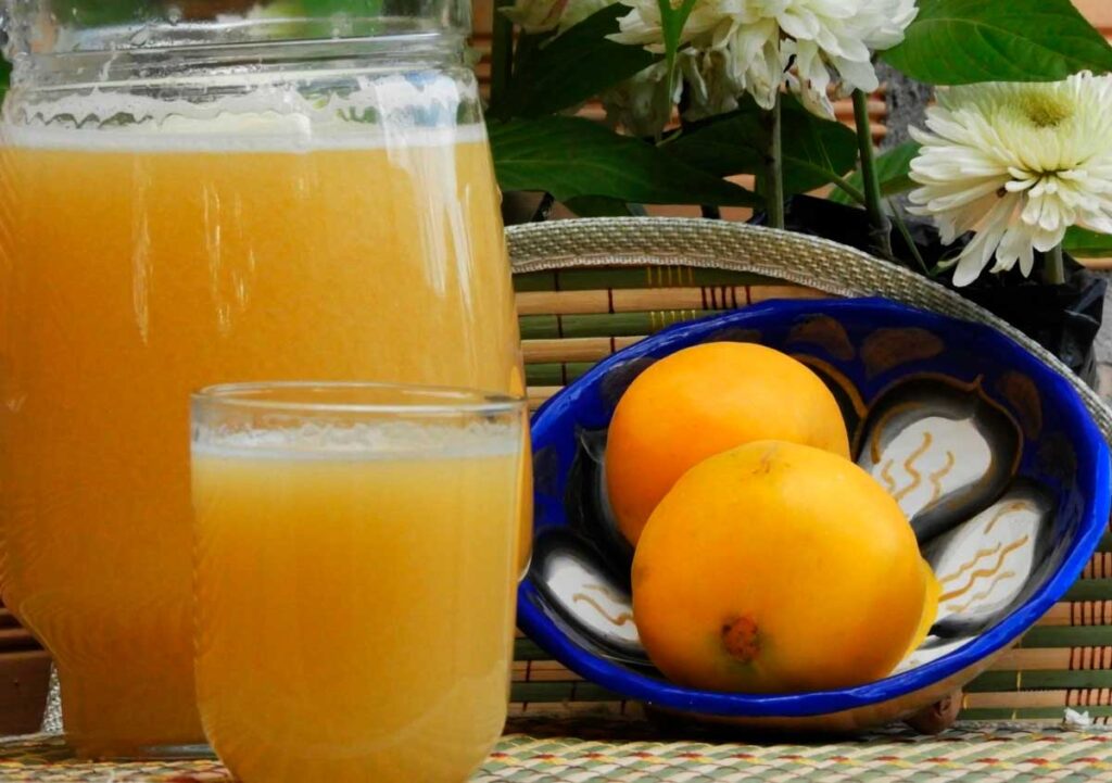 Jarra y vaso reales de zumo de arazá junto a dos frutos